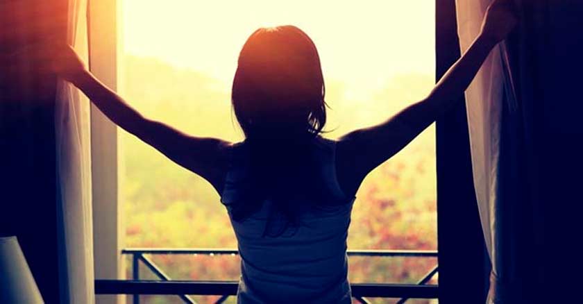 mujer quitando las cortinas de una ventana para ver la luz del amanecer