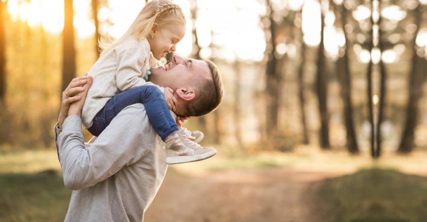 padre cargando a su hija felices en medio del bosque 