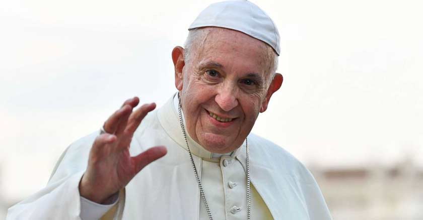 papa francisco mira directamente a la camara con una sonrisa y saluda fondo claro 