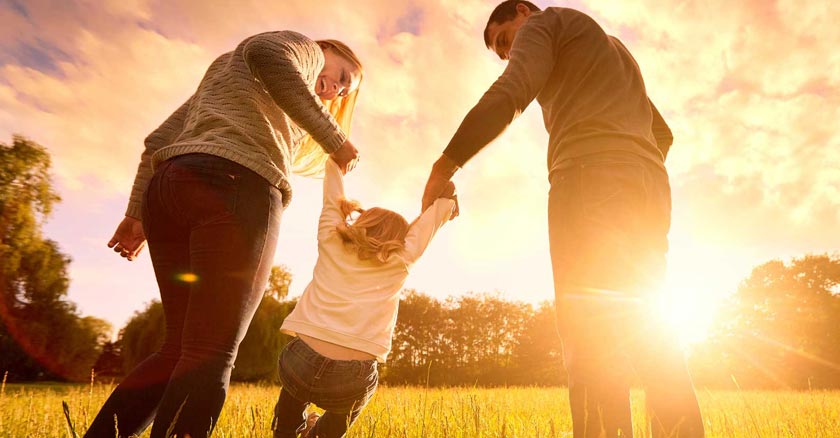 esposos sosteniendo a su hija de las manos campo ocaso sol brillante dia