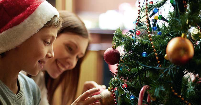 familia reunida madre hijo frente arbol de navidad sotiendo adornos navidenos