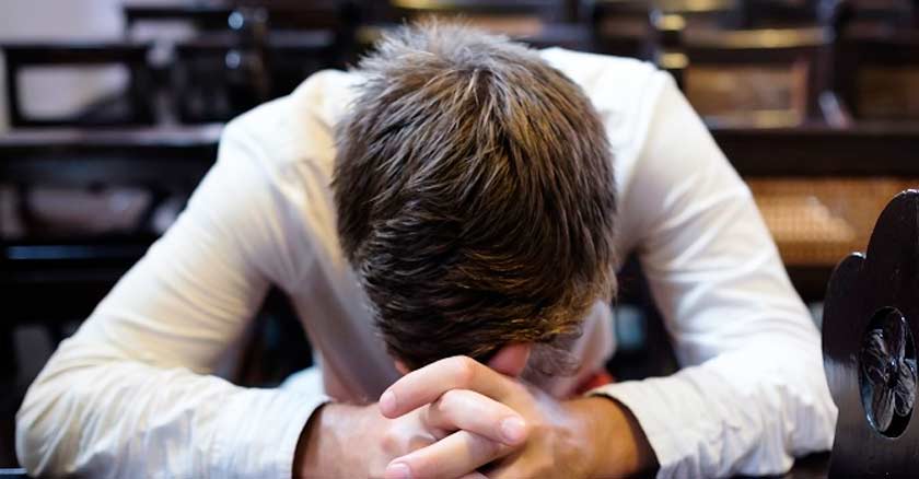 hombre con la cabeza postrada en actitud de oracion orando banco de misa