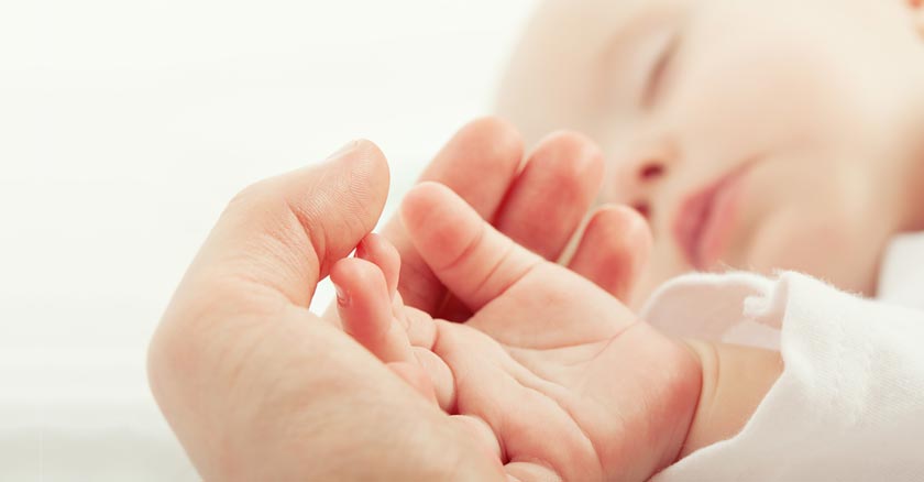 mano de papa sosteniendo mano de bebe dormido acostado dia 