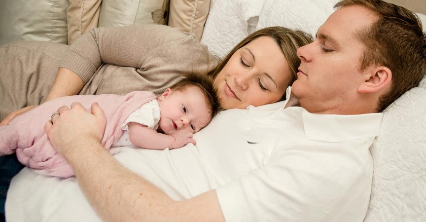 papa mama y bebe acostados durmiendo en cama dia 