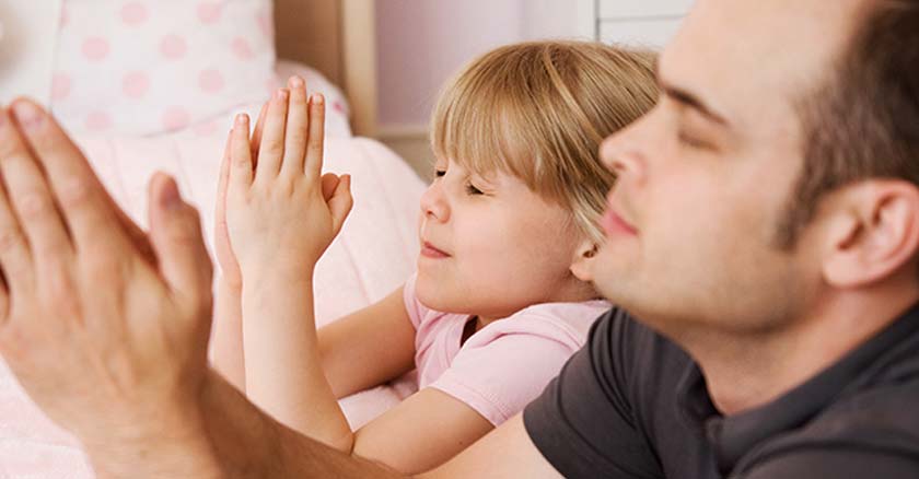 papa orando junto a su hija al lado de su cama ojos cerrados manos juntas oracion